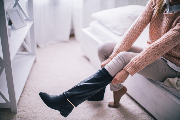 Boots on Young woman sitting at the bed in her bedroom, getting ready for work, putting on her boots.